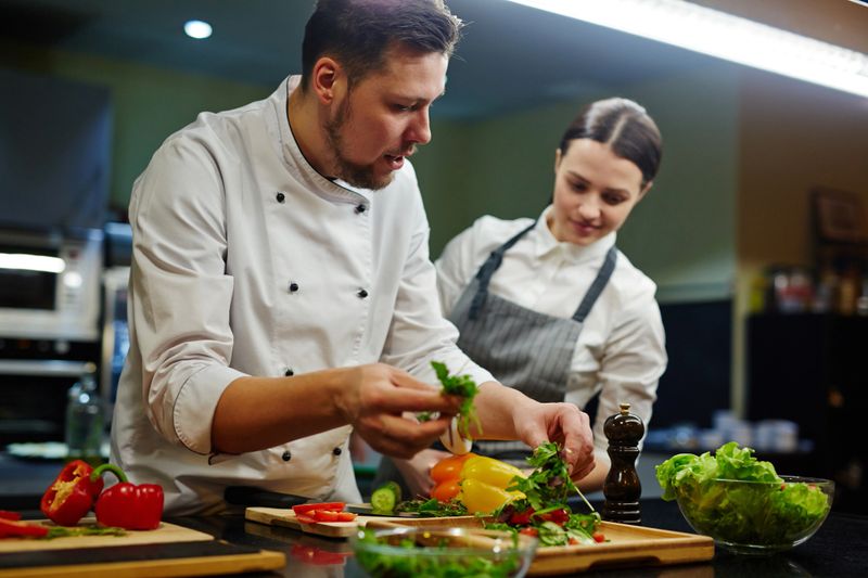 Chef consulting his trainee while cooking salad