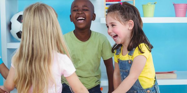 Children holding hands and laughing together in a bright playroom