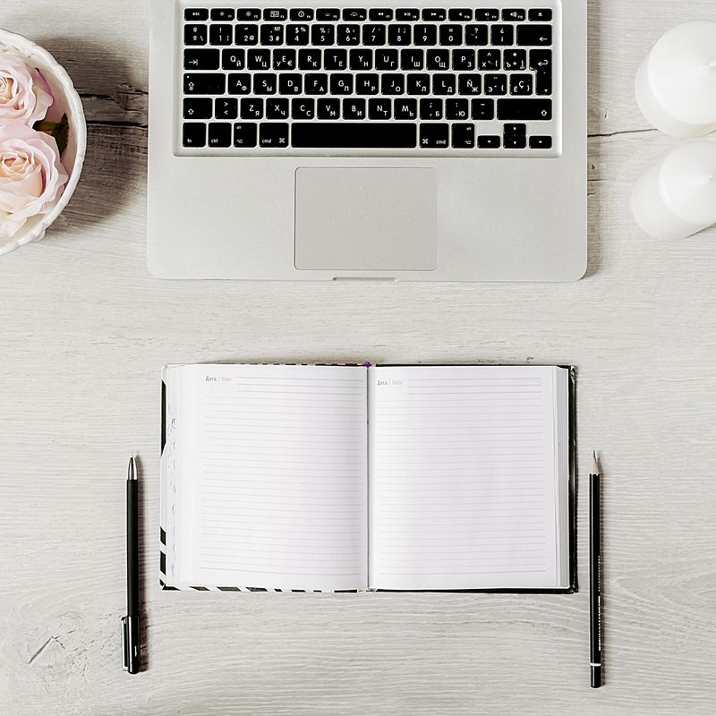 Workplace in modern style with laptop, diary, white candles, roses and wooden desk. Flat lay