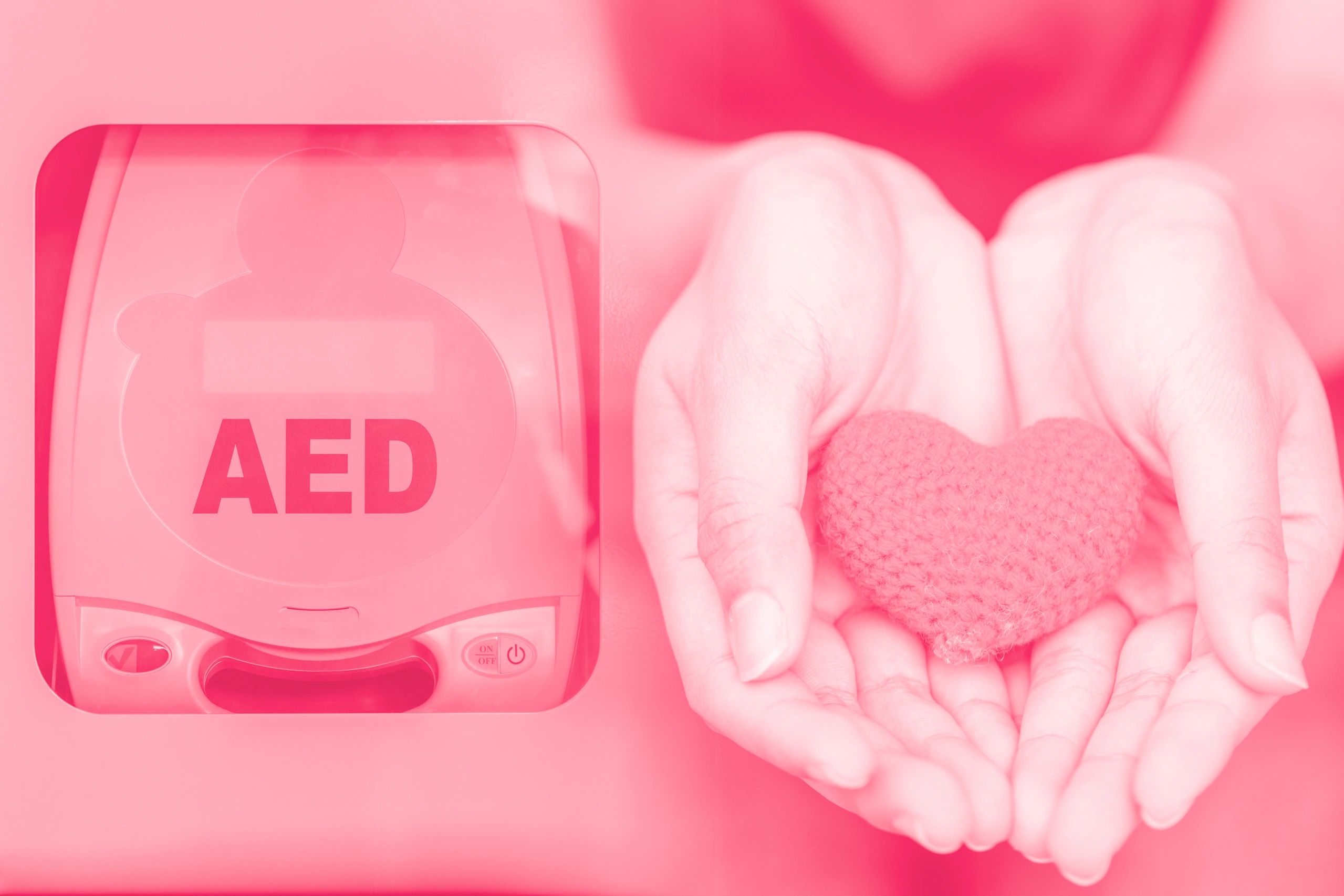 AED device beside hands holding a red heart symbol.
