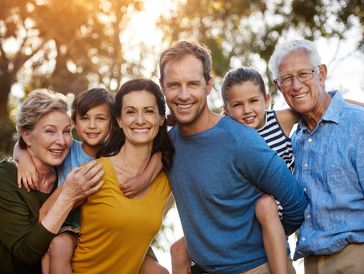 A multi-generational family all looking at the camera and smiling. Arms around each other.