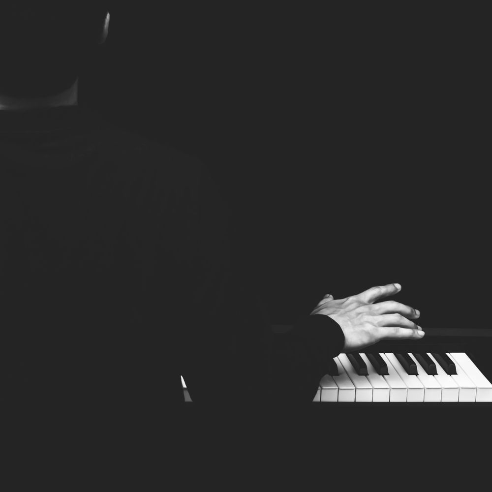 A person playing piano with hands poised above keys in low light.