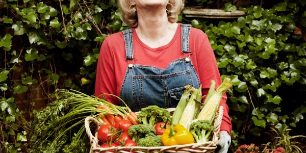 Woman holding basket of fresh vegetables in garden.