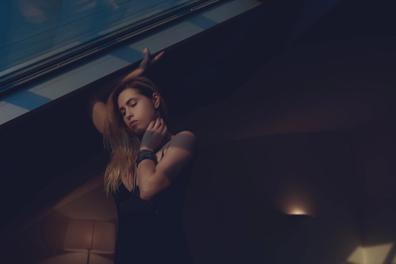 attractive blond hair woman in the morning time in black dress touching her hair  and posing with eyes closed. tranquil scene.
