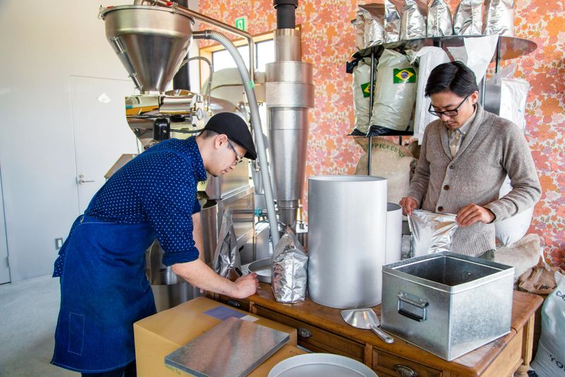 Two coffee roasters working in their workshop. Sorting, packaging and stacking bags of freshly roasted beans. Okayama, Japan. March 2017