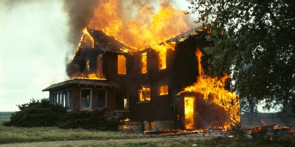 A large house engulfed in intense flames and thick smoke.