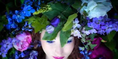 Woman with closed eyes surrounded by vibrant flowers and green leaves.