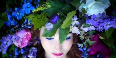 Woman with closed eyes surrounded by vibrant flowers and green leaves.