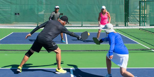 Four people playing pickleball on an outdoor court in sunny weather.
