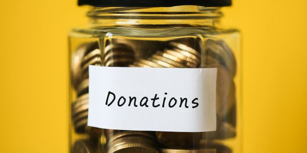 A jar labeled Donations filled with coins against a yellow background.