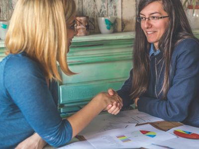 Two women shaking hands over business charts during a meeting.