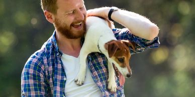 Man joyfully holding a small dog outdoors.