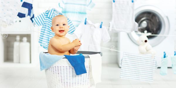 Happy baby sitting in laundry basket with clothes drying.