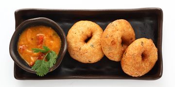 Three vadas with chutney served on a black rectangular plate.