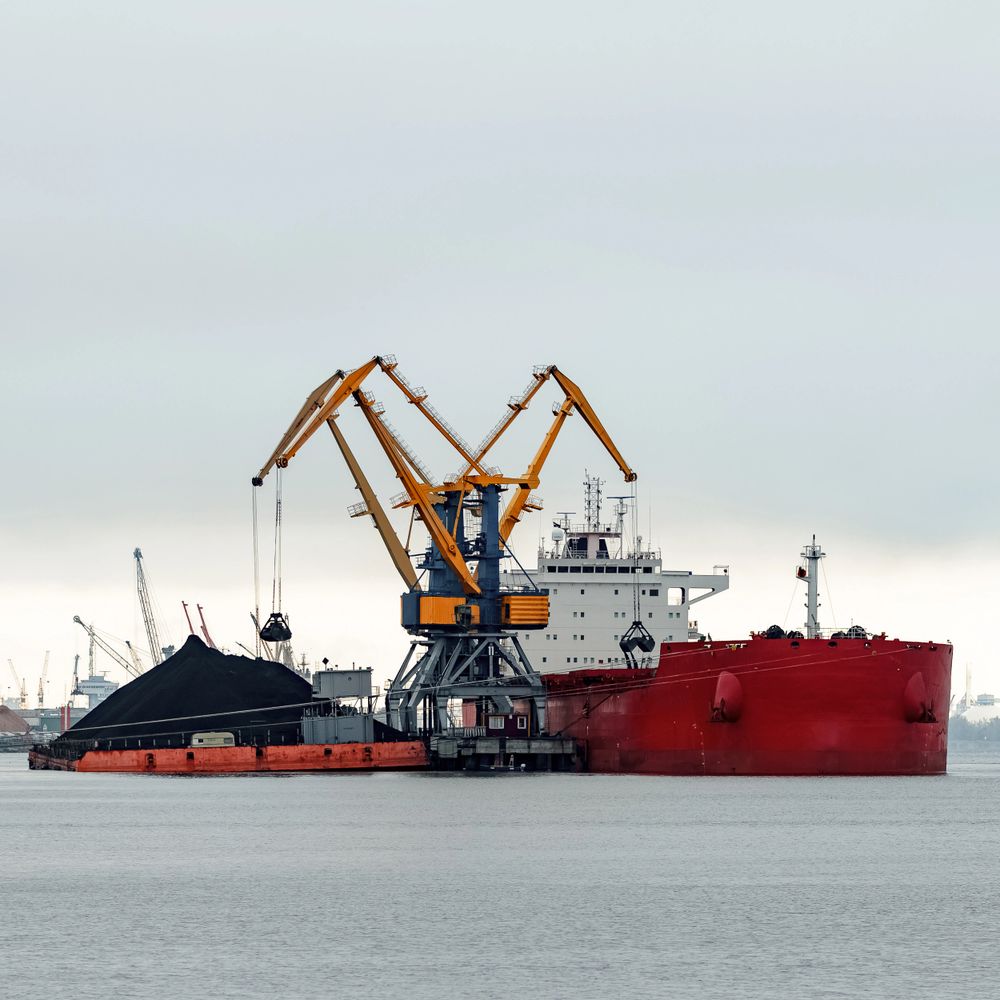 Cargo ship being loaded with coal at a port using large cranes.