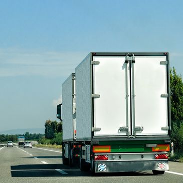 Two white cargo trucks driving on a highway under a clear blue sky.