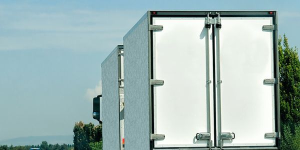 White semi-truck driving on a highway with clear blue sky.