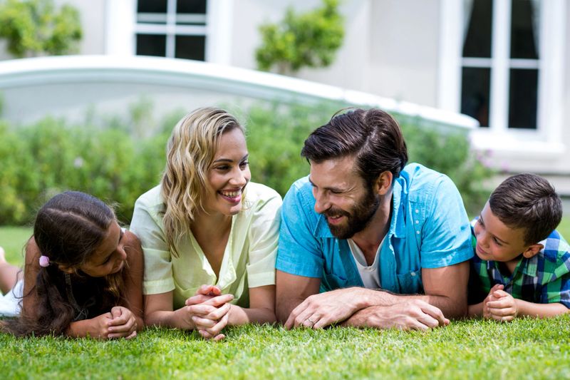 Close-up of smiling parents with children lying on grass in yard