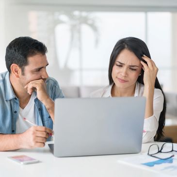 A man and woman look concerned while discussing something on a laptop.