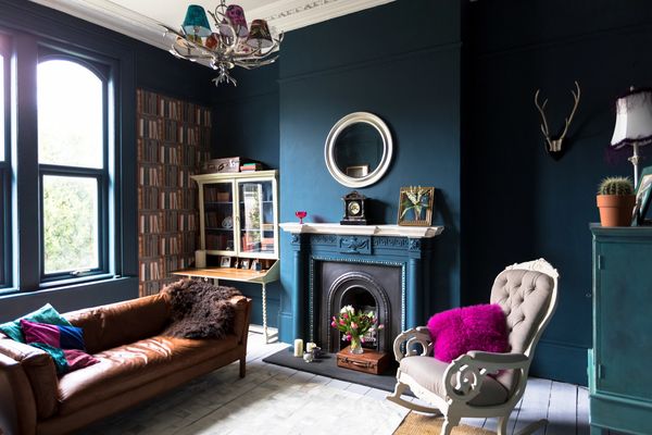 Cozy living room with dark teal walls, vintage furniture, and colorful accents.