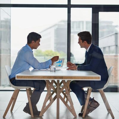 Two men in business attire discussing charts on a tablet in an office.