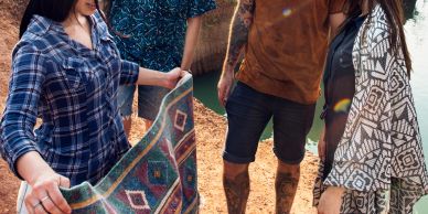 Four people examining a colorful woven rug outdoors.