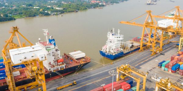 Cargo ships docked at a busy port with yellow cranes and containers.