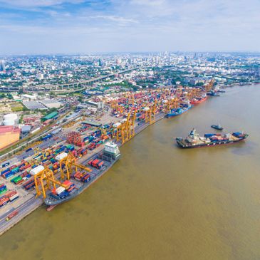 A busy shipping port with cranes and cargo ships along a river in a sprawling city.