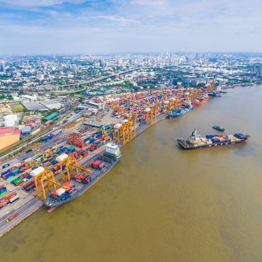 A busy container port with ships and cranes along the river near a city.