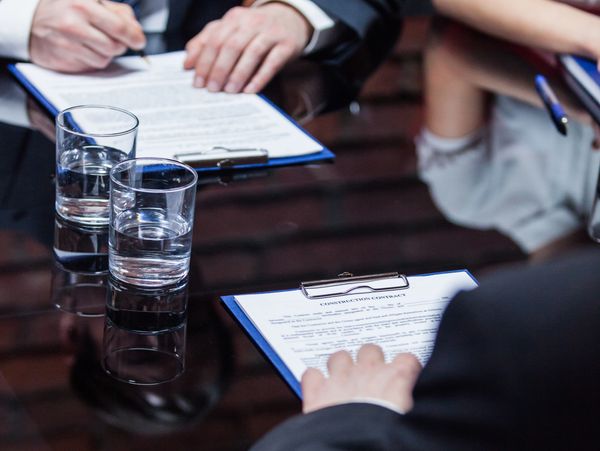 Professionals reviewing and signing construction contracts at a meeting.