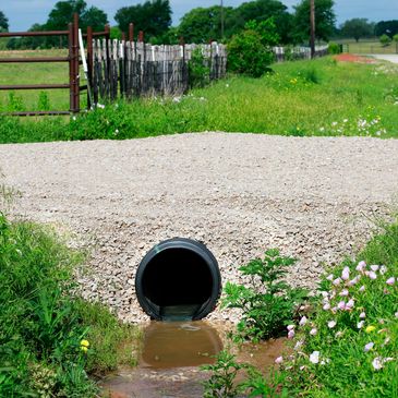 Drainage pipe in rural area surrounded by greenery.