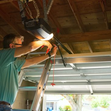 Man repairing a garage door opener on a ladder inside a garage.