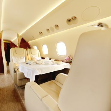 Luxurious private jet interior with elegant dining setup and beige leather seats.