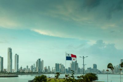 Panama City skyline with national flags in the foreground under a cloudy sky.