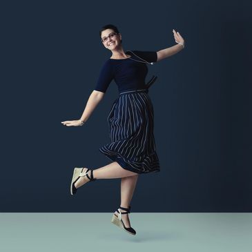 Woman joyfully jumping in a navy outfit against a dark background.