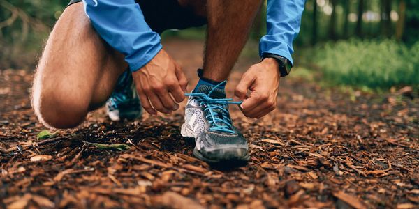 Person tying running shoes on a forest trail.
