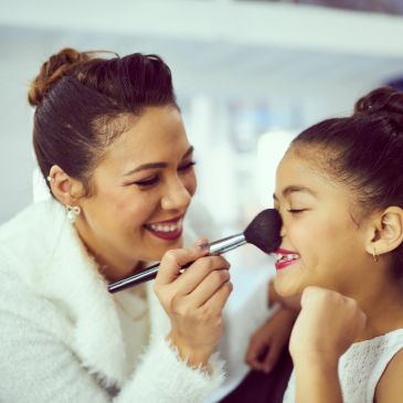 Woman applying makeup on a smiling girl.