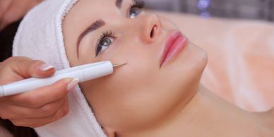 Woman receiving facial treatment with a handheld device.