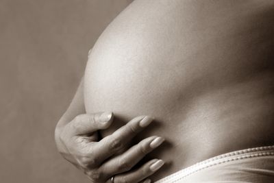 Close-up of a pregnant belly with hands cradling it.