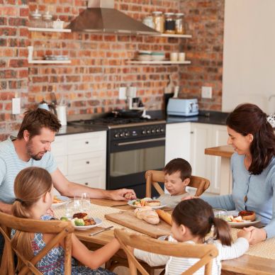 Family of five praying together before a meal in their kitchen.
