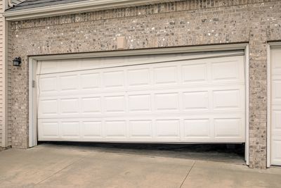 Damaged garage door cables and bottom brackets: frayed steel ropes on bent metal brackets.
