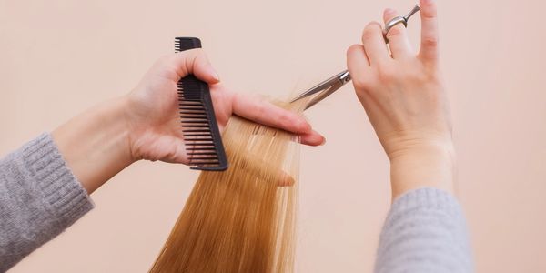 Hands cutting blonde hair with scissors and comb.