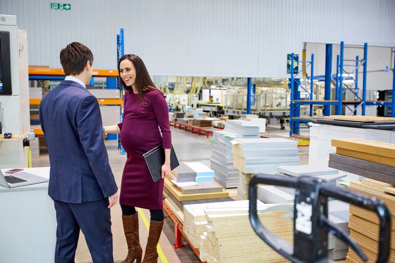 Young pregnant businesswoman having a friendly conversation with male colleague on factory shopfloor