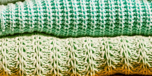 Stack of two textured knitted blankets in green and cream colors.