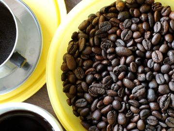 Close-up of coffee beans with brewed coffee and a filter on yellow plates.