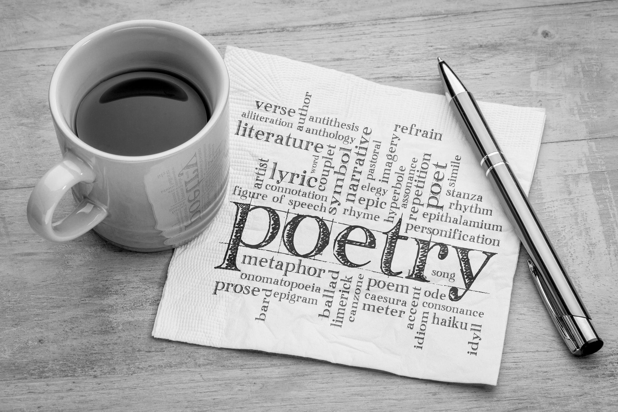 Coffee cup, napkin with poetry words, and pen on wooden table.