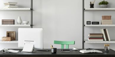 Minimalist workspace with green chair, shelves, and computer on black desk.