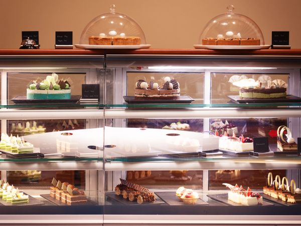 A display case filled with various cakes and pastries under glass covers.