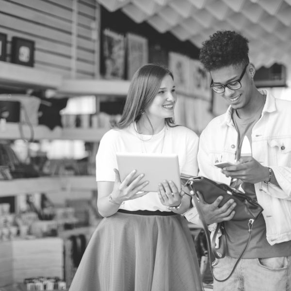 Two young people using a tablet and smartphone in a store, smiling and interacting.