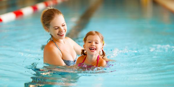 Mother teaching daughter to swim in pool.